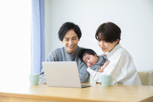 赤ちゃんを抱きながらパソコンを見る夫婦